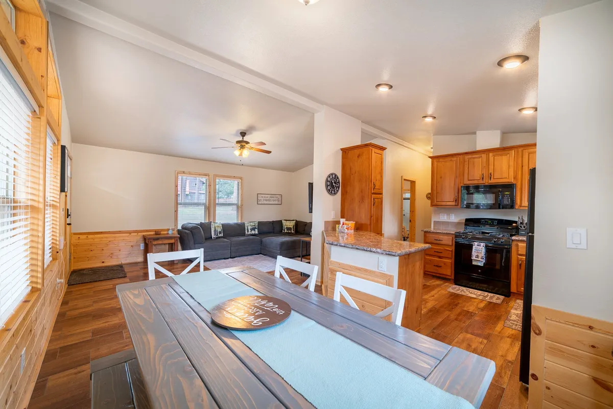 A cozy open-plan interior featuring a dining table set for a group, a comfortable sofa in the background, and a kitchen island. The arrangement encourages social connection, making it easy to transition between dining, relaxing, and cooking together.