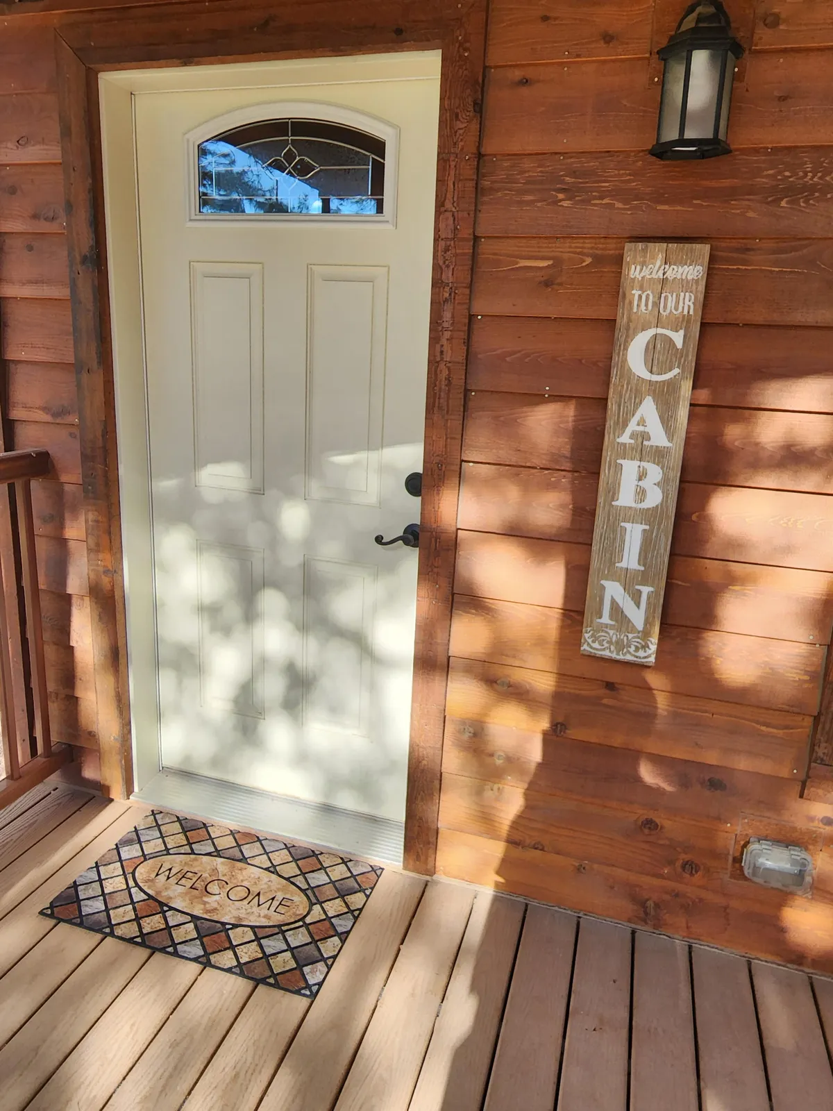 This inviting exterior shot features the cabin’s front door, welcome sign, and a cozy welcome mat. The scene gives a warm, inviting first impression of the property and its readiness to greet all guests—including furry ones.