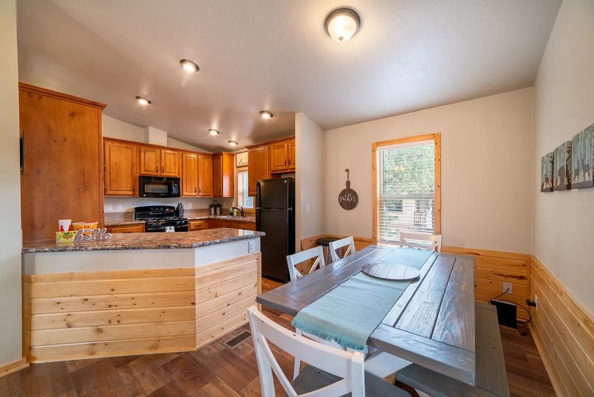 A warm and cozy kitchen and dining area featuring a kitchen island, a wooden dining table set for a group, and rustic wooden cabinetry. The space is bathed in soft, inviting lighting, perfect for both social gatherings and intimate meals with family or friends.