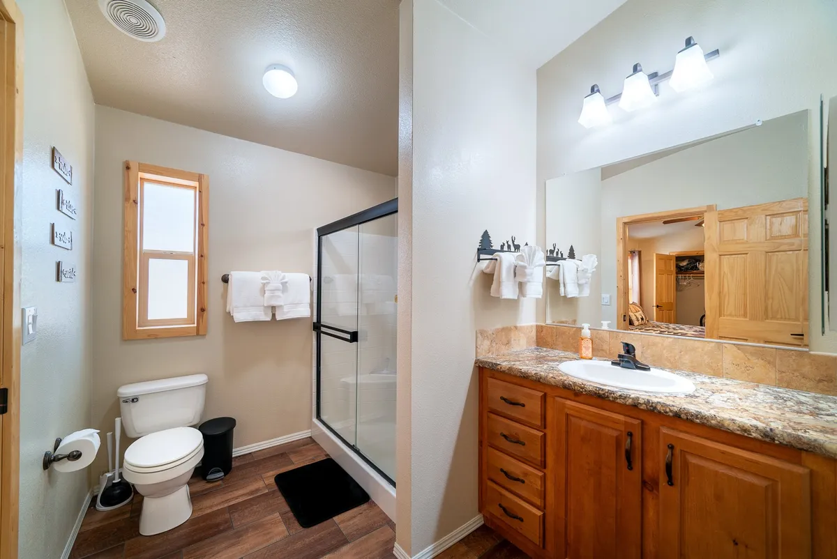A bright bathroom scene with a modern shower, a spacious vanity with a sink, wooden cabinetry, and natural light from a nearby window. The space is clean, serene, and inviting, perfect for relaxing routines.