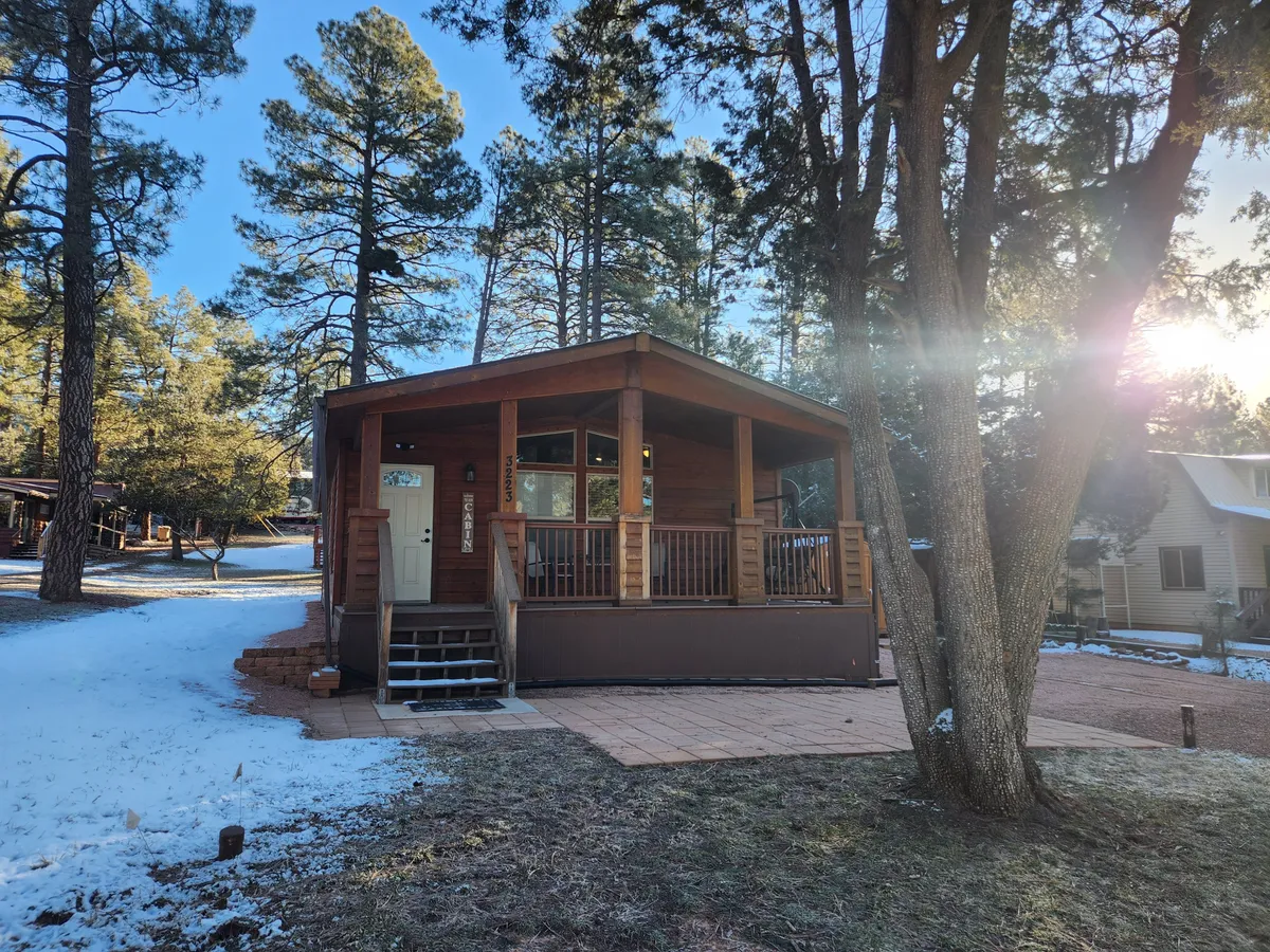 A welcoming log cabin with a wooden porch overlooks a snow-dusted landscape framed by tall trees. The cozy porch offers ample space to relax and enjoy the natural beauty, with the cabin architecture exuding warmth and rustic charm. The sunset is often visible from the porch, making it a perfect spot for quiet moments together.