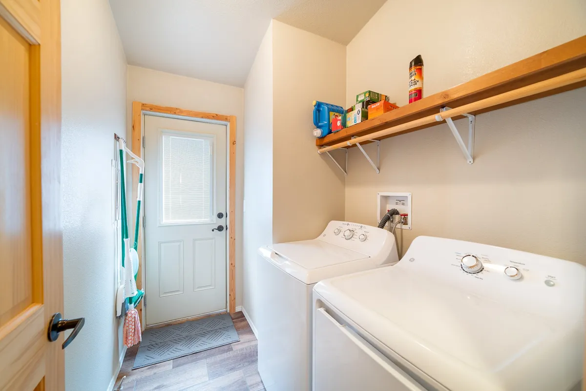 A functional laundry area featuring washing machines, open shelving with supplies, and an open door that hints at accessibility and ease of use.