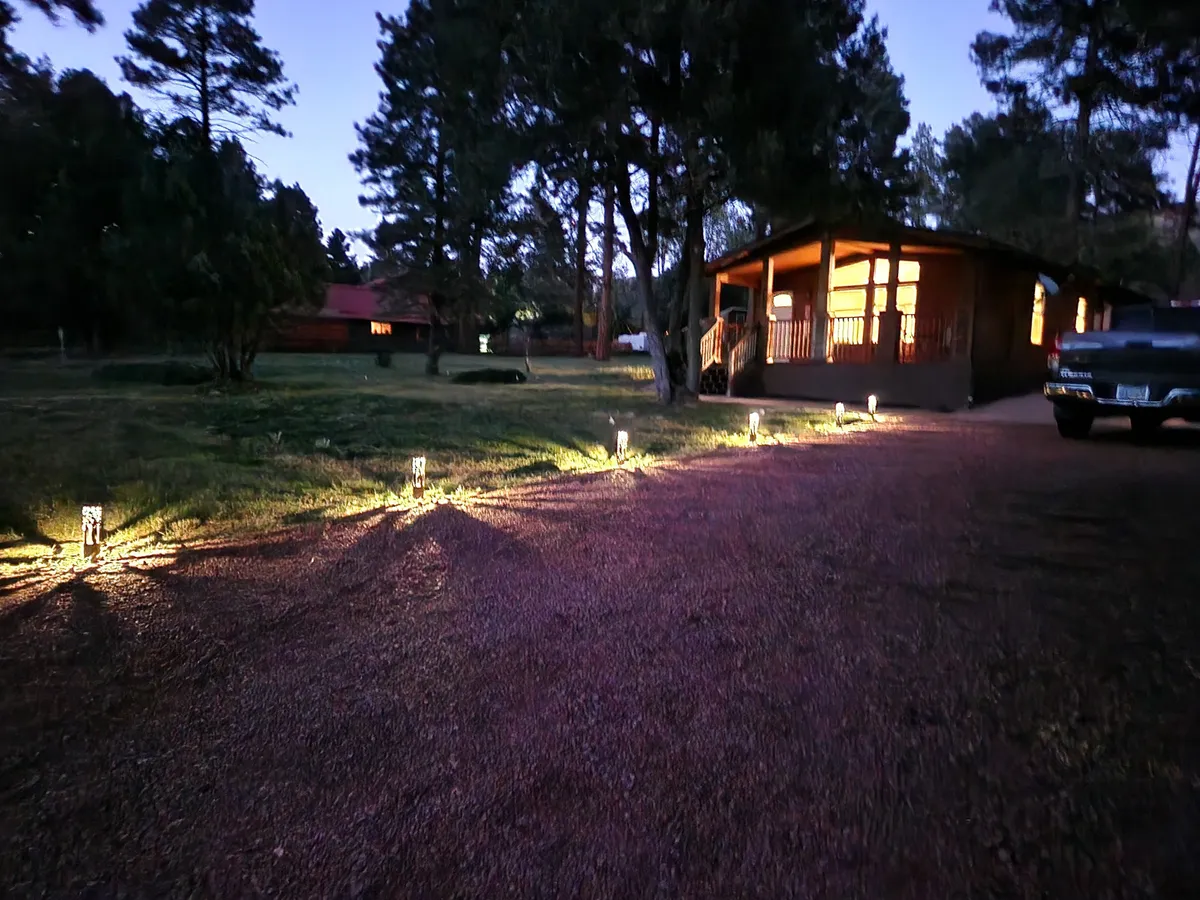 This image features the front porch of the property with warmly illuminated windows, pathway lights, and surrounding trees. The welcoming glow creates a sense of gathering and relaxation, hinting at evenings spent together after a day of exploring. The composition offers both a sense of arrival and a connection to the peaceful outdoors.